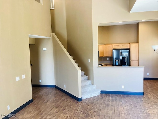 kitchen featuring black refrigerator with ice dispenser, dark wood-type flooring, a towering ceiling, and baseboards