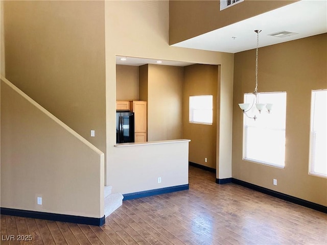 empty room featuring visible vents, baseboards, stairway, hardwood / wood-style floors, and an inviting chandelier