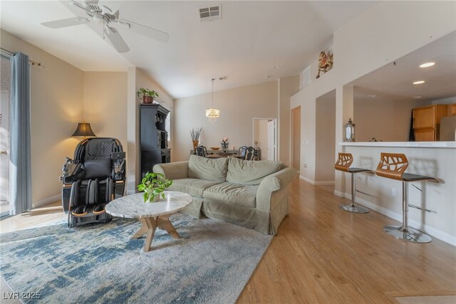 living room with visible vents, baseboards, ceiling fan, light wood-style flooring, and vaulted ceiling