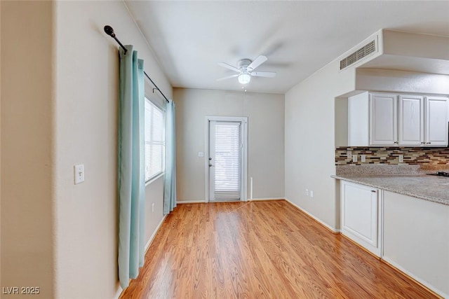 kitchen with light wood finished floors, visible vents, white cabinets, ceiling fan, and backsplash