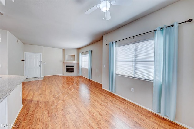 unfurnished living room with light wood-type flooring, a fireplace, and ceiling fan