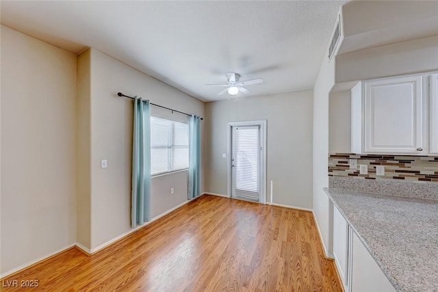 interior space featuring ceiling fan, visible vents, white cabinetry, decorative backsplash, and light wood finished floors