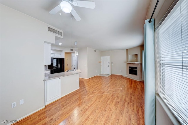 unfurnished living room with visible vents, light wood-style flooring, a ceiling fan, a sink, and a tile fireplace