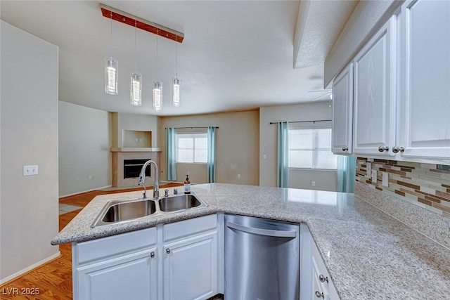 kitchen featuring stainless steel dishwasher, open floor plan, white cabinets, a sink, and a peninsula