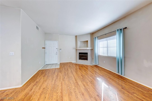 unfurnished living room with light wood-type flooring, visible vents, baseboards, and a tile fireplace