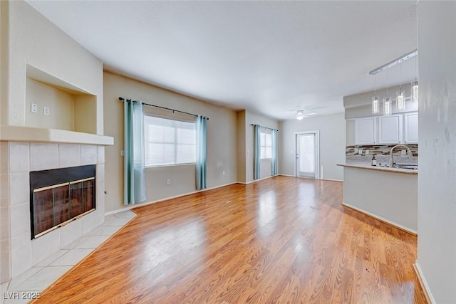 unfurnished living room with ceiling fan, a fireplace, a sink, and light wood-style flooring