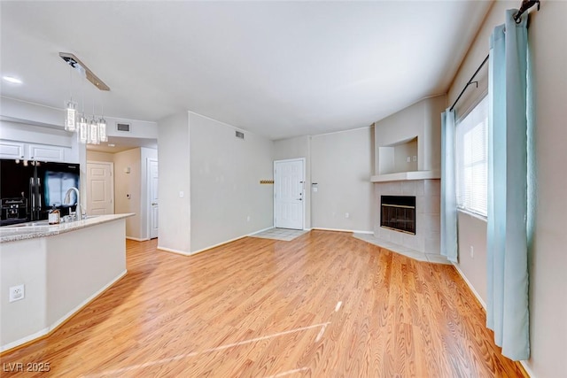 unfurnished living room with baseboards, visible vents, light wood finished floors, and a tiled fireplace