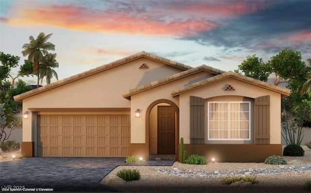 mediterranean / spanish house featuring an attached garage, a tiled roof, decorative driveway, and stucco siding