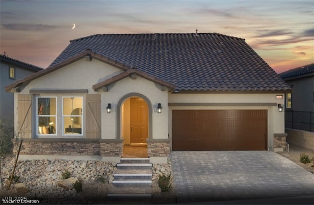 view of front of home with a garage, stone siding, a tiled roof, decorative driveway, and stucco siding