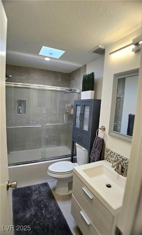 bathroom featuring a skylight, shower / bath combination with glass door, tasteful backsplash, toilet, and vanity