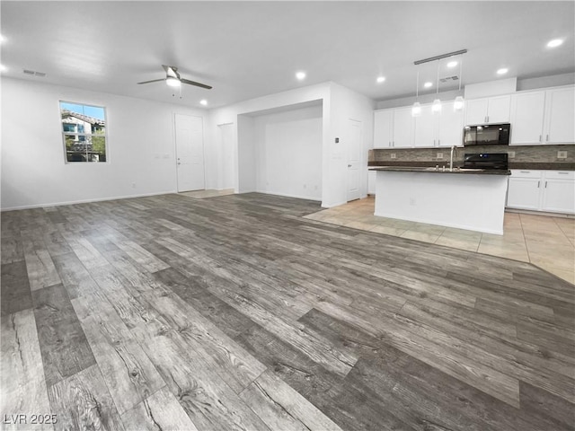 kitchen with pendant lighting, dark countertops, open floor plan, white cabinets, and black appliances