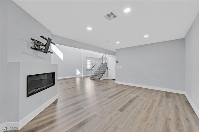 unfurnished living room featuring visible vents, baseboards, a glass covered fireplace, light wood-style flooring, and stairway