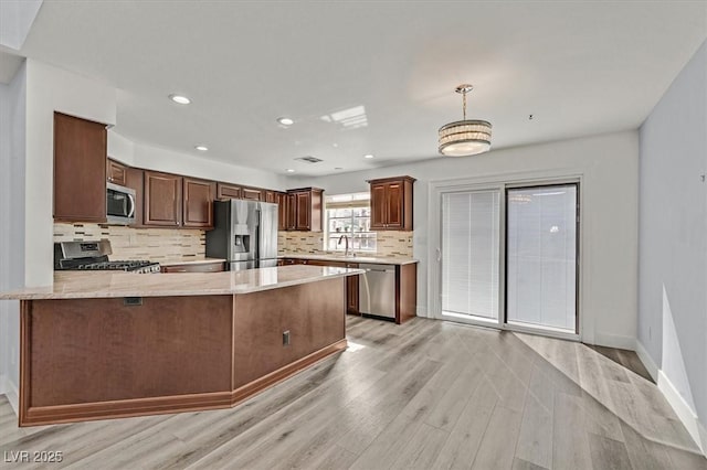 kitchen featuring hanging light fixtures, light wood-style flooring, appliances with stainless steel finishes, a sink, and a peninsula