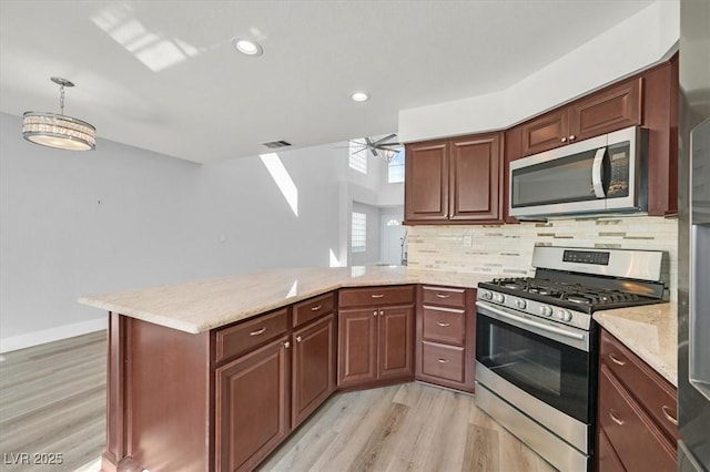 kitchen featuring visible vents, a peninsula, hanging light fixtures, stainless steel appliances, and backsplash