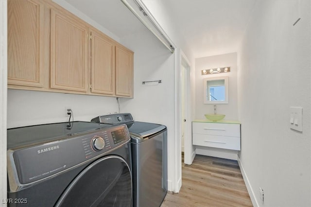 laundry room with cabinet space, baseboards, light wood-type flooring, washing machine and dryer, and a sink