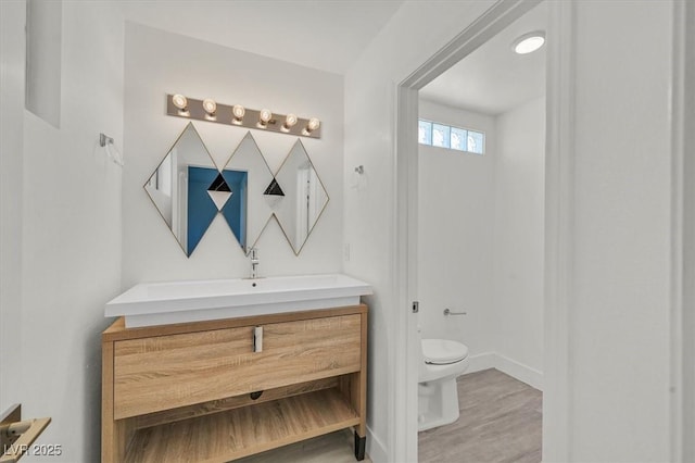 bathroom featuring toilet, baseboards, wood finished floors, and vanity