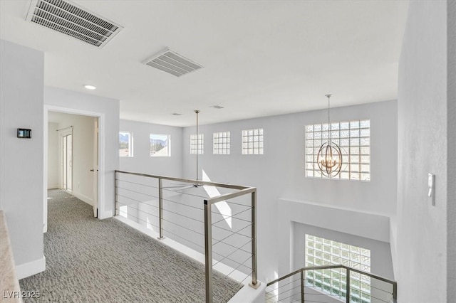 hall with a chandelier, visible vents, an upstairs landing, and carpet flooring