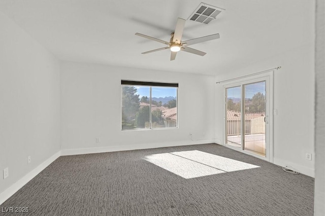 spare room with ceiling fan, dark carpet, visible vents, and baseboards