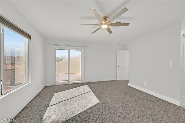 unfurnished room with attic access, dark carpet, baseboards, and a ceiling fan