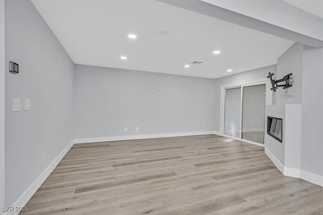 unfurnished living room with recessed lighting, light wood-type flooring, a glass covered fireplace, and baseboards