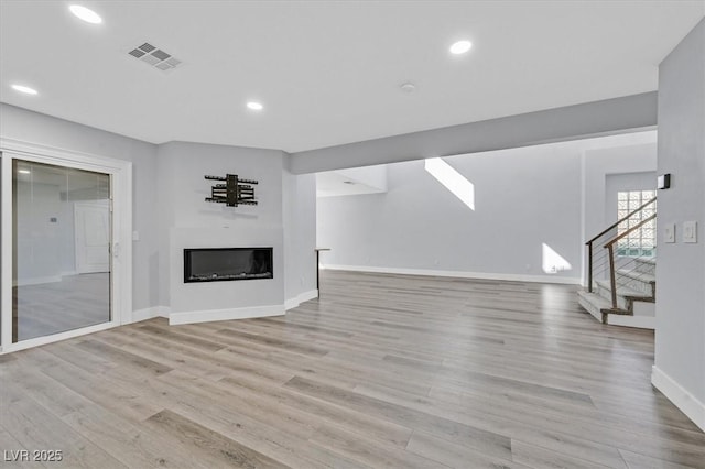 unfurnished living room with visible vents, light wood-style flooring, stairway, a glass covered fireplace, and baseboards