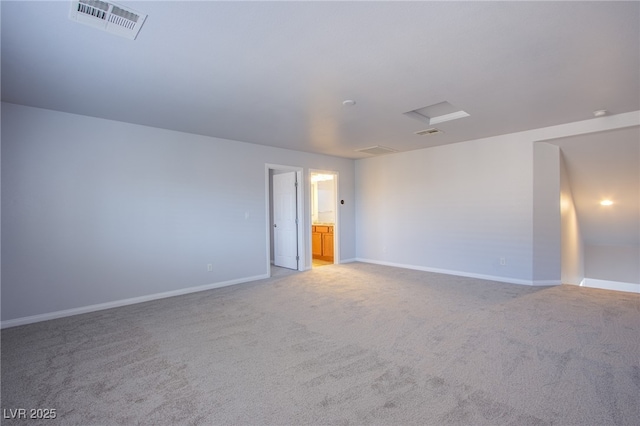 carpeted empty room featuring baseboards, visible vents, and attic access