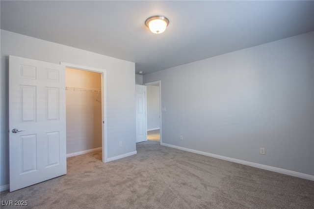 unfurnished bedroom with a spacious closet, a closet, light colored carpet, and baseboards