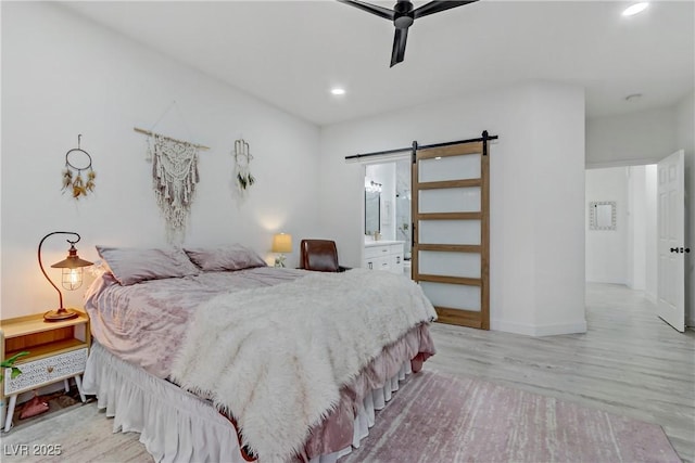 bedroom featuring a barn door, light wood-type flooring, ensuite bath, and recessed lighting