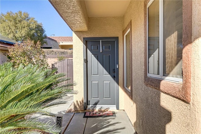 view of exterior entry with fence and stucco siding