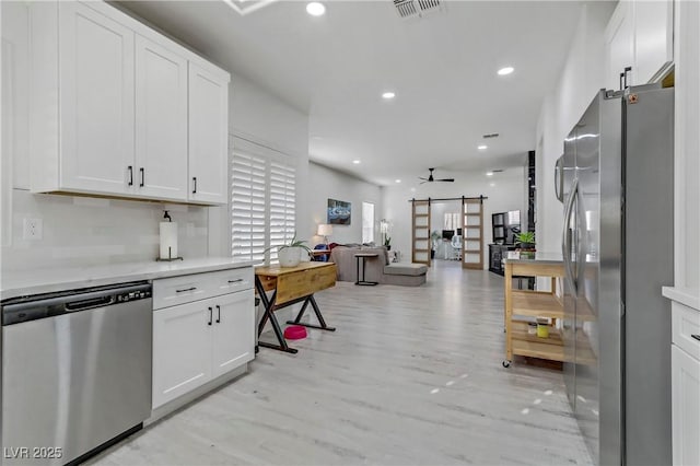 kitchen with stainless steel appliances, light countertops, a barn door, open floor plan, and white cabinets