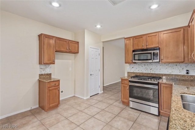 kitchen with light stone counters, light tile patterned flooring, decorative backsplash, appliances with stainless steel finishes, and brown cabinets