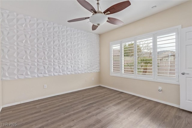 empty room featuring ceiling fan, baseboards, and wood finished floors