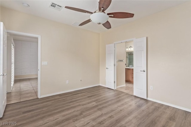 unfurnished bedroom with connected bathroom, wood finished floors, visible vents, and baseboards