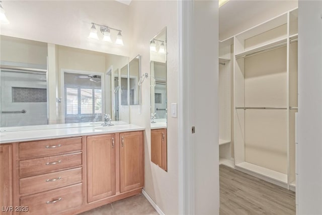 full bathroom with wood finished floors, a spacious closet, ceiling fan, and vanity