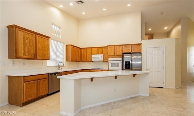 kitchen with a center island, stainless steel appliances, light countertops, a towering ceiling, and a kitchen breakfast bar