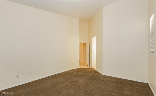 unfurnished room with dark colored carpet, a towering ceiling, and baseboards