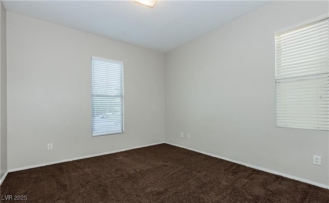 spare room featuring dark colored carpet and baseboards