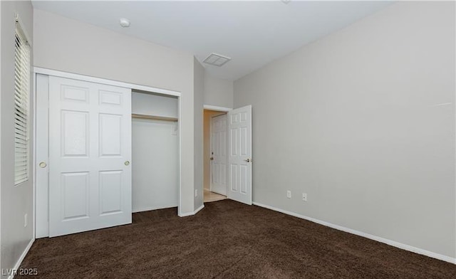 unfurnished bedroom featuring baseboards, visible vents, dark colored carpet, and a closet