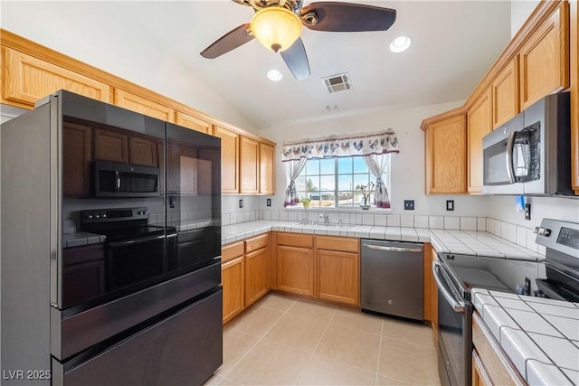 kitchen with lofted ceiling, stainless steel appliances, a sink, visible vents, and tile counters