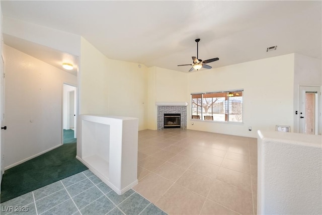 unfurnished living room featuring a glass covered fireplace, visible vents, ceiling fan, and light tile patterned floors