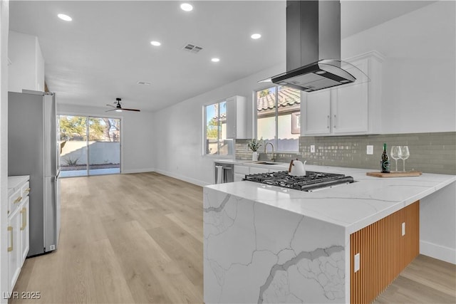 kitchen with appliances with stainless steel finishes, a peninsula, light stone countertops, island exhaust hood, and white cabinetry