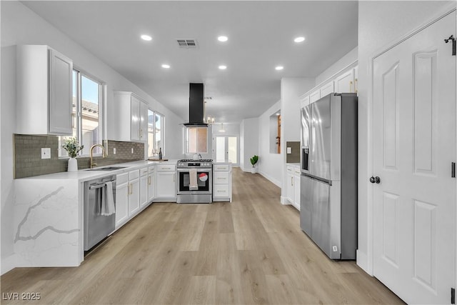 kitchen with visible vents, appliances with stainless steel finishes, white cabinets, a sink, and island range hood