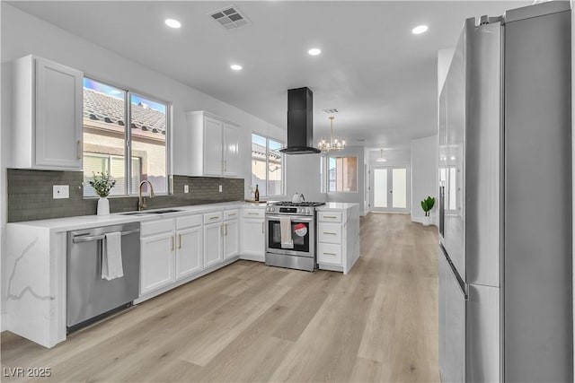 kitchen with appliances with stainless steel finishes, white cabinets, light countertops, and island exhaust hood