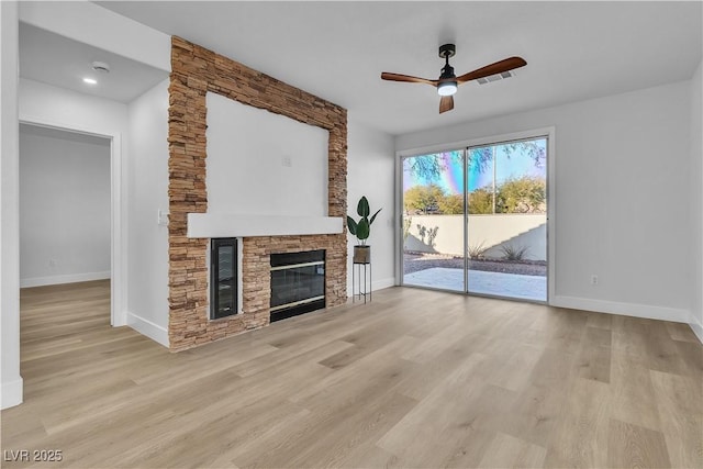 unfurnished living room featuring light wood-style floors, visible vents, a stone fireplace, and baseboards