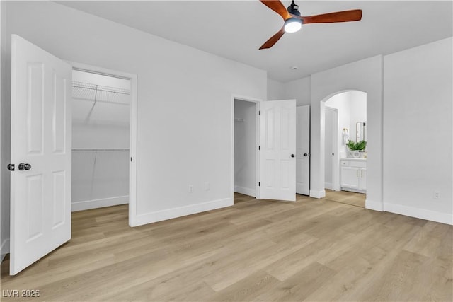 unfurnished bedroom featuring arched walkways, light wood-style flooring, and baseboards