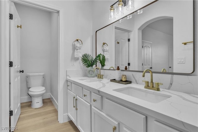 full bathroom with wood finished floors, a sink, toilet, and double vanity