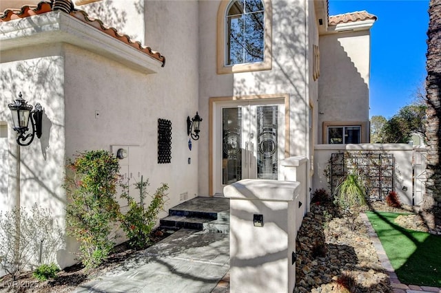 entrance to property with a tile roof, fence, and stucco siding