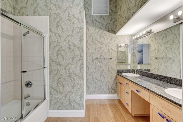 bathroom featuring shower / bath combination with glass door, visible vents, a sink, and wallpapered walls