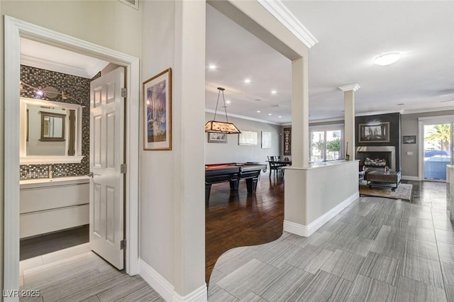 hall featuring light wood-type flooring, ornate columns, baseboards, and crown molding