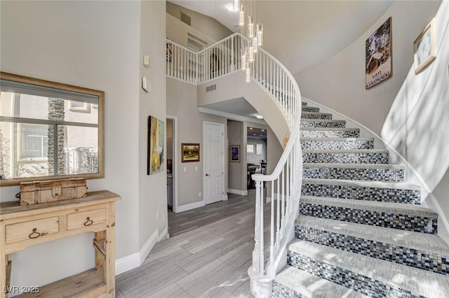 stairway with visible vents, a towering ceiling, baseboards, and wood finished floors